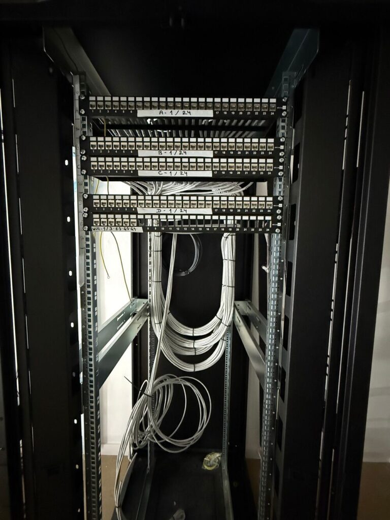 Installation de baie de brassage et câblage réseau structuré Baie de brassage avec panneaux A-D et Wi-Fi, câbles Ethernet blancs organisés dans une armoire réseau.