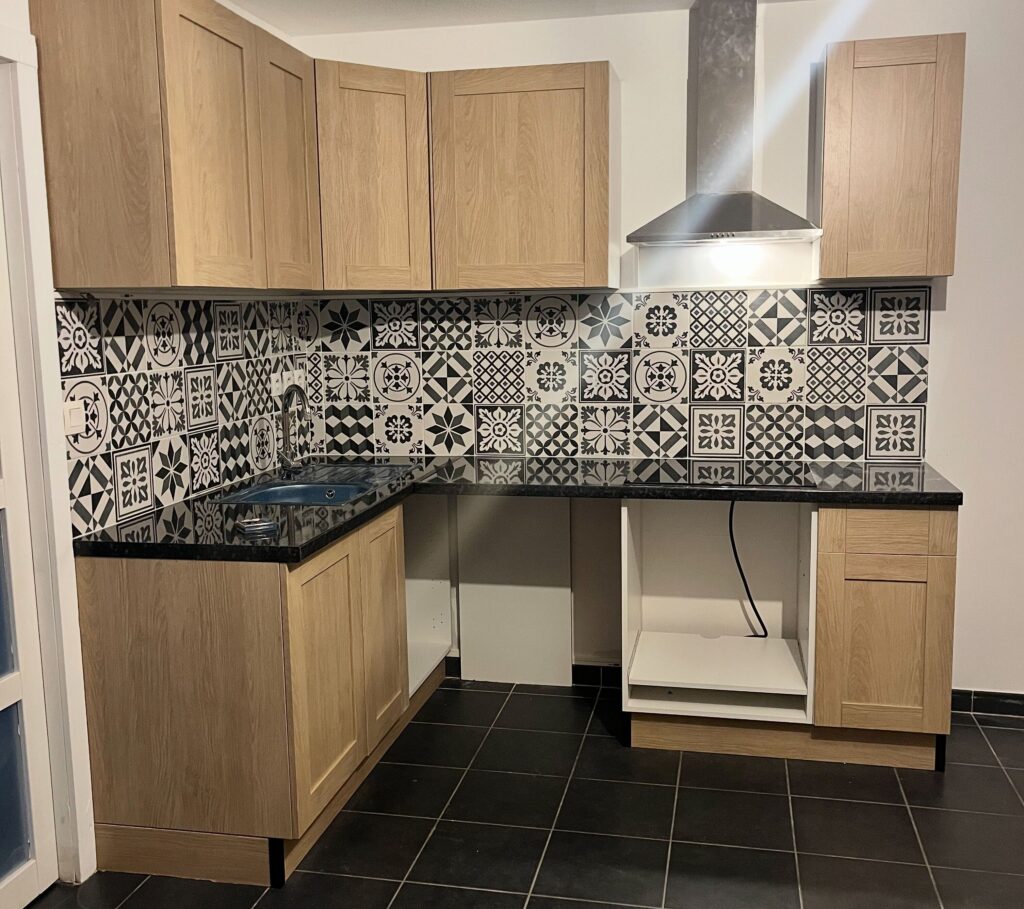 Cuisine Moderne : Bois Clair et Crédence Noir et Blanc Cuisine moderne avec meubles en bois clair, crédence à motifs noir et blanc et plan de travail en granit noir.