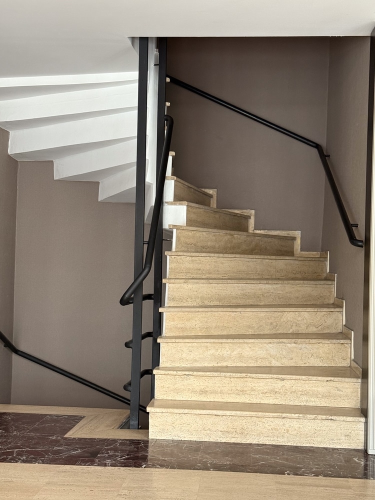 Escalier intérieur moderne en pierre beige et rampe noire Escalier intérieur en pierre beige avec rampe en métal noir et marches tournantes sur mur taupe.