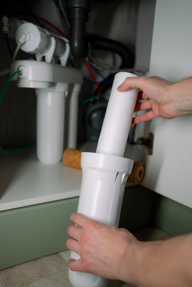 Remplacement de filtre à eau sous évier : guide pratique Mains remplaçant une cartouche de filtre à eau blanche dans son boîtier sous un évier de cuisine.