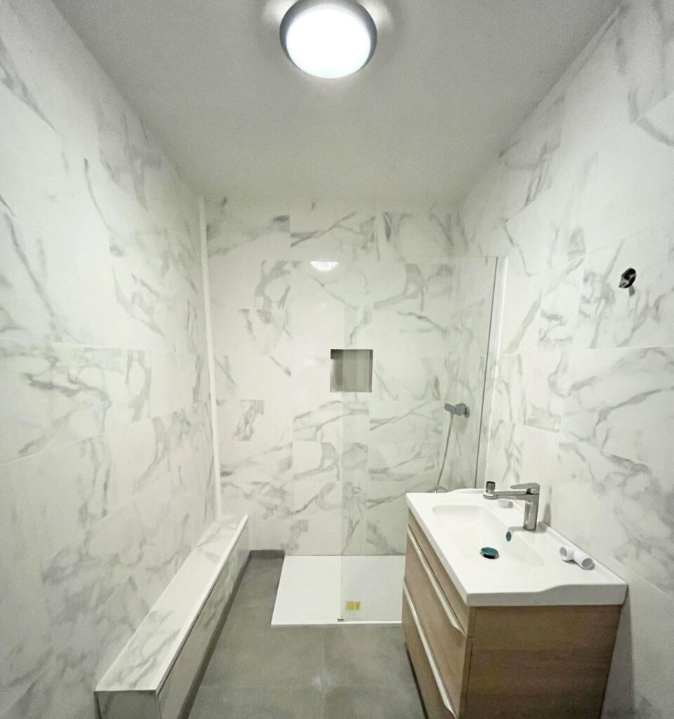 Salle de Bain Moderne en Marbre avec Douche Italienne Salle de bain moderne avec carrelage effet marbre blanc, douche à l'italienne et meuble vasque en bois clair.