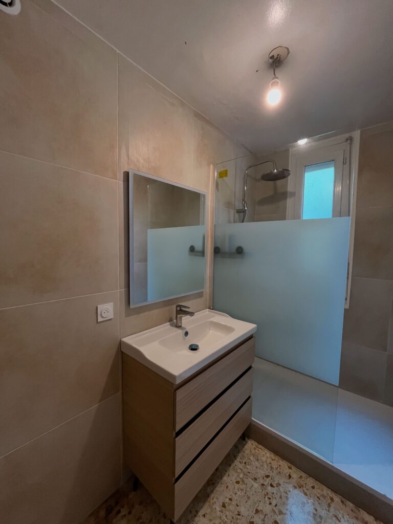 Salle de bain moderne avec douche et meuble vasque bois Salle de bain moderne avec meuble vasque en bois, douche à l'italienne, paroi dépolie et carrelage beige clair.