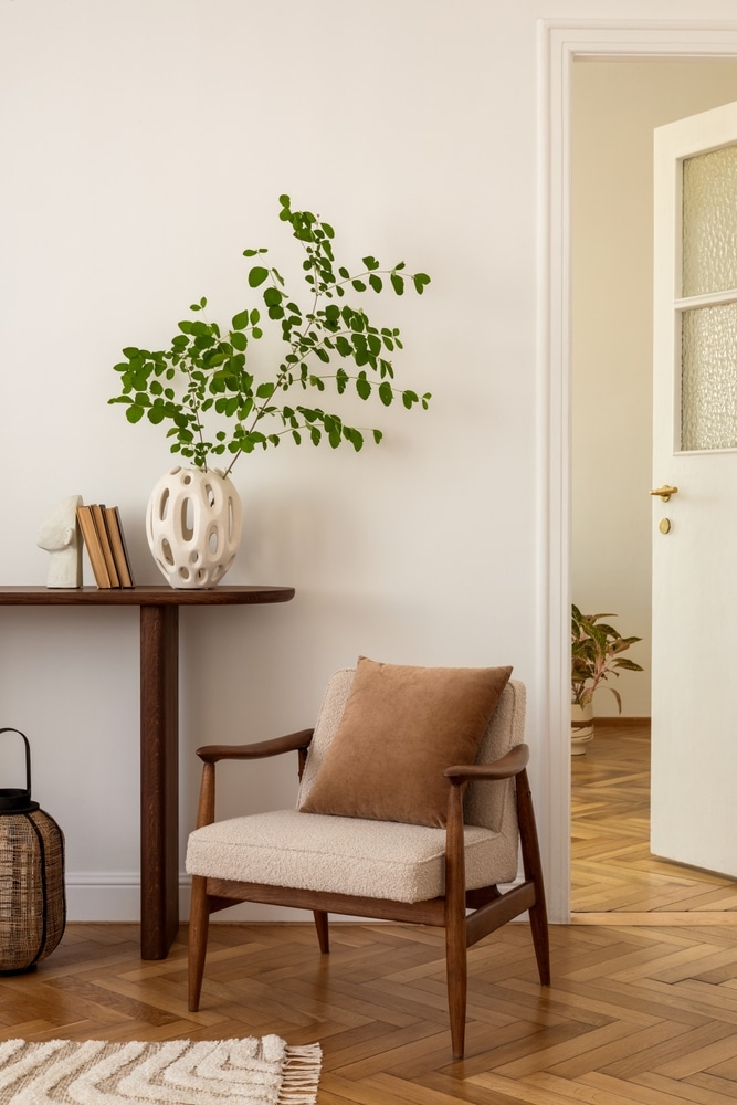 Décoration Intérieure Scandinave avec Fauteuil et Bois Fauteuil scandinave beige, vase blanc sculptural et branches vertes dans un salon au parquet en chevrons.